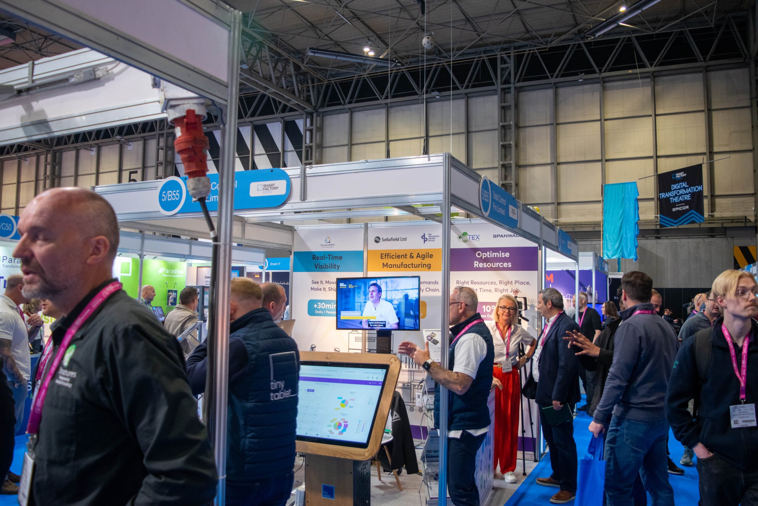 Smart Manufacturing WEek 2025, the "Total Control Pro Limited" stand with screens, promotional materials, and a seating area, alongside other exhibition booths.